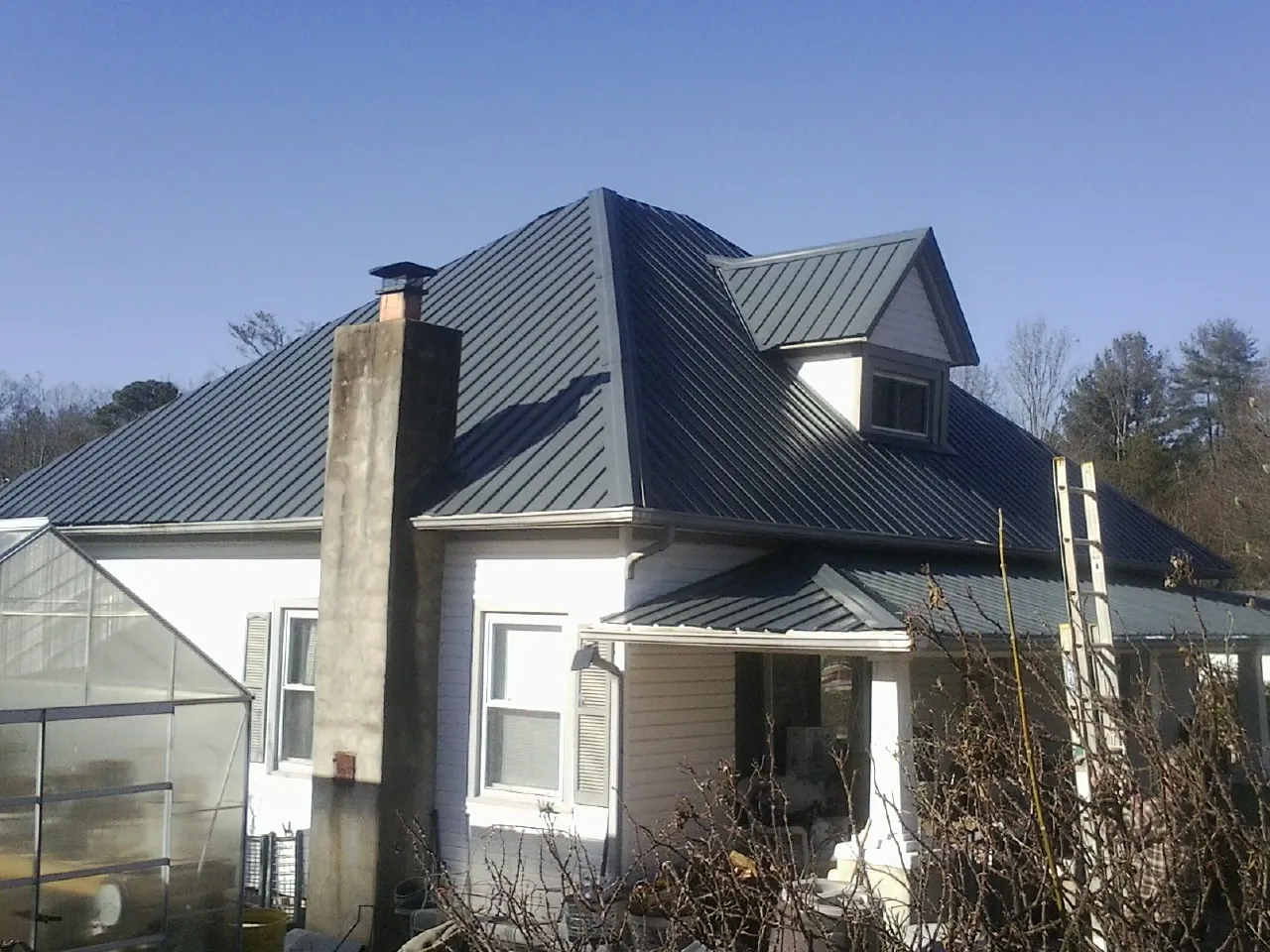 Dark blue standing seam metal roof on a white farmhouse with dormer — Slate & Tile Roof Repair by Roofing Brothers in Rewey