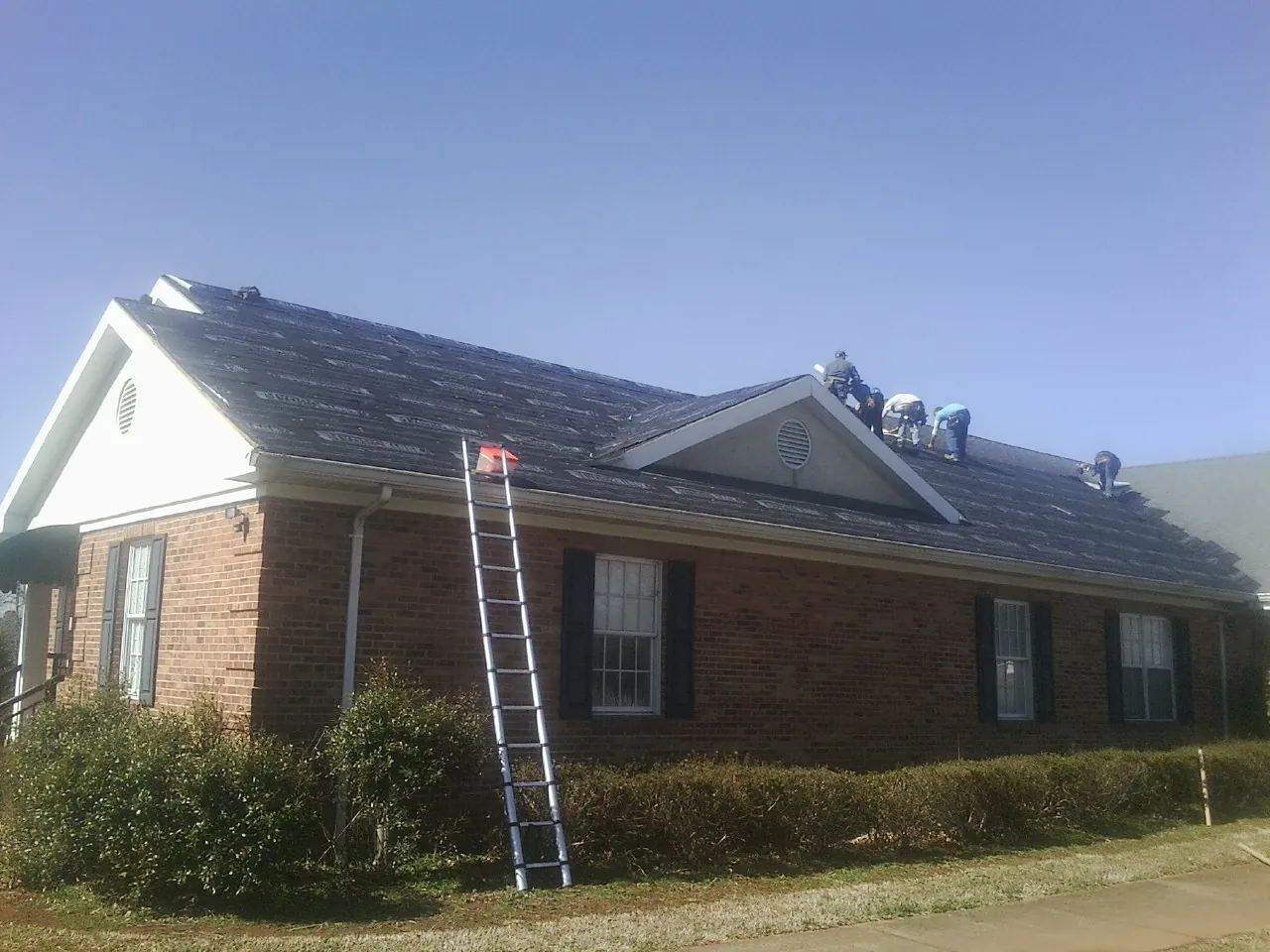Crew tearing shingles off a brick ranch roof with a ladder set — Metal Roof Repair work by our crew in Rewey