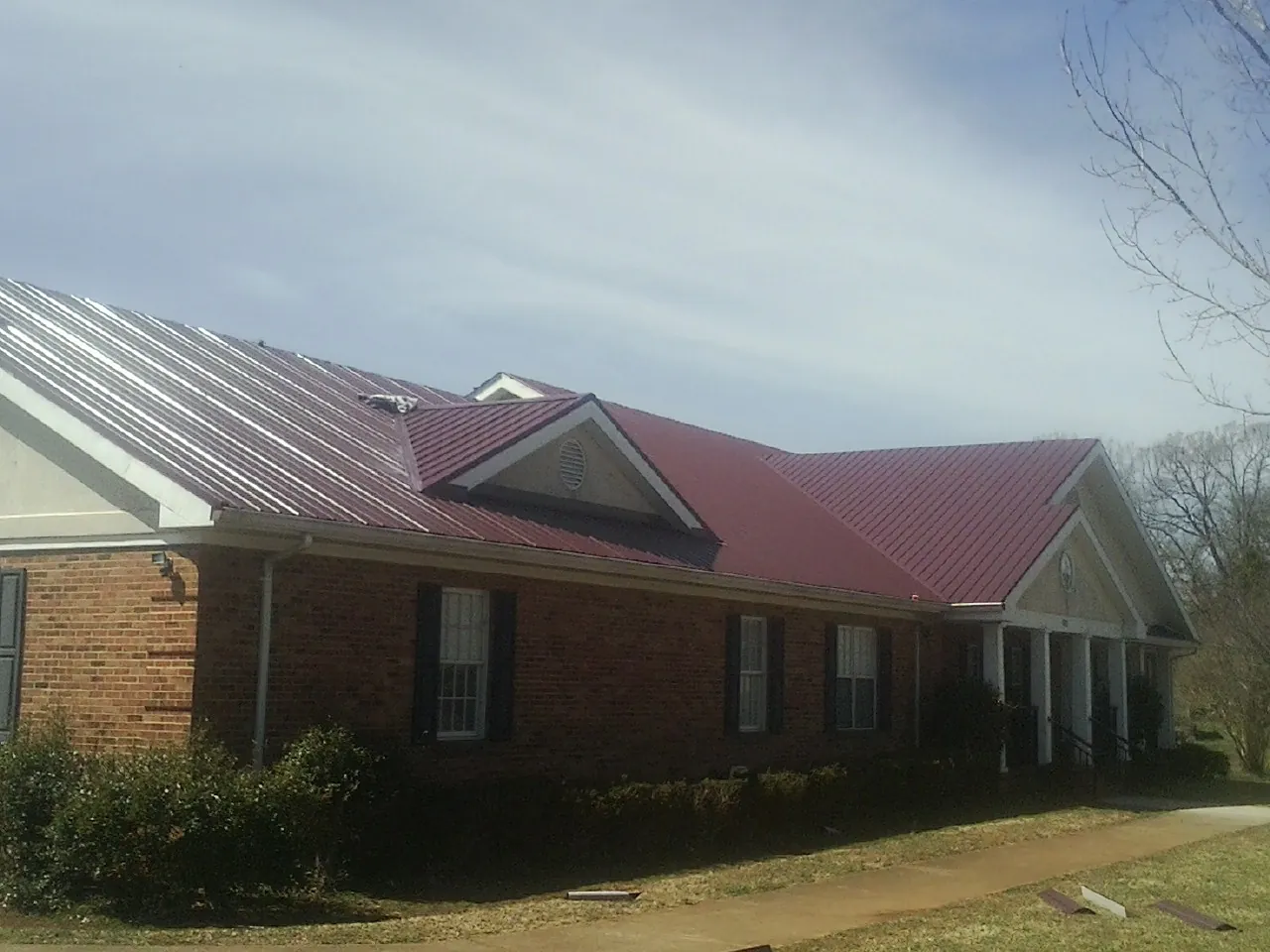 Red metal roof with gabled entries on a long brick building, from a Hail Damage Roof Repair job in Rewey