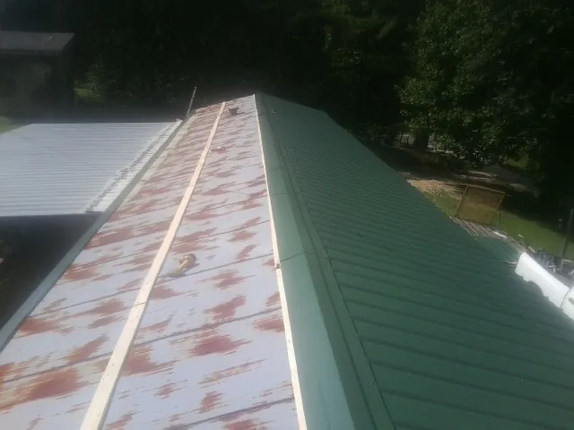 Old rusted panels beside newly installed green metal roofing — Wind Damage Roof Repair by Roofing Brothers in Rewey