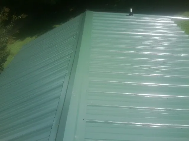New green metal panels meeting at the ridge of a roof — Flat Roof Repair work by our crew in Rewey