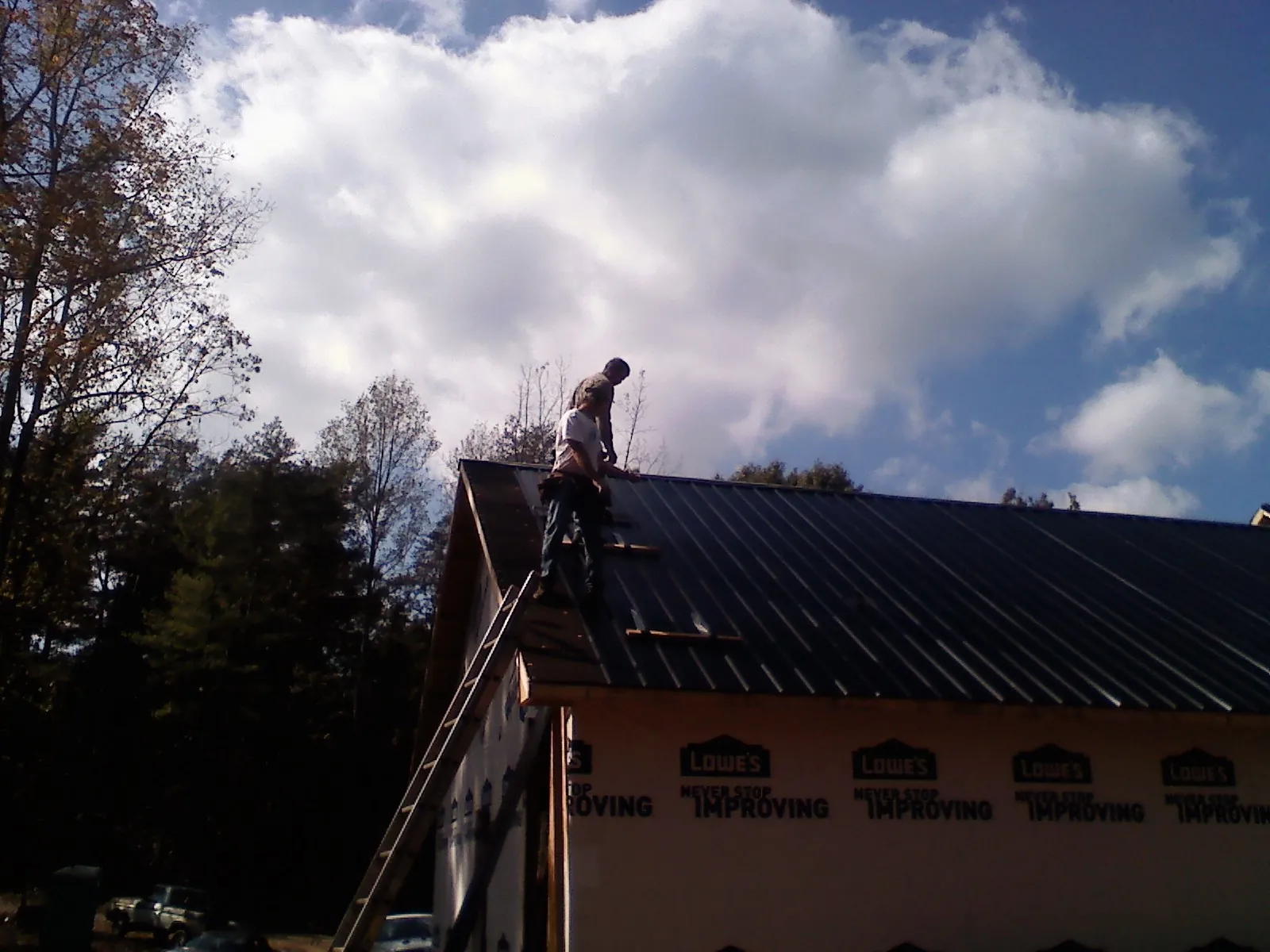 Roofer fastening dark metal panels high against a cloudy sky, from a Roof Inspection job in Rewey